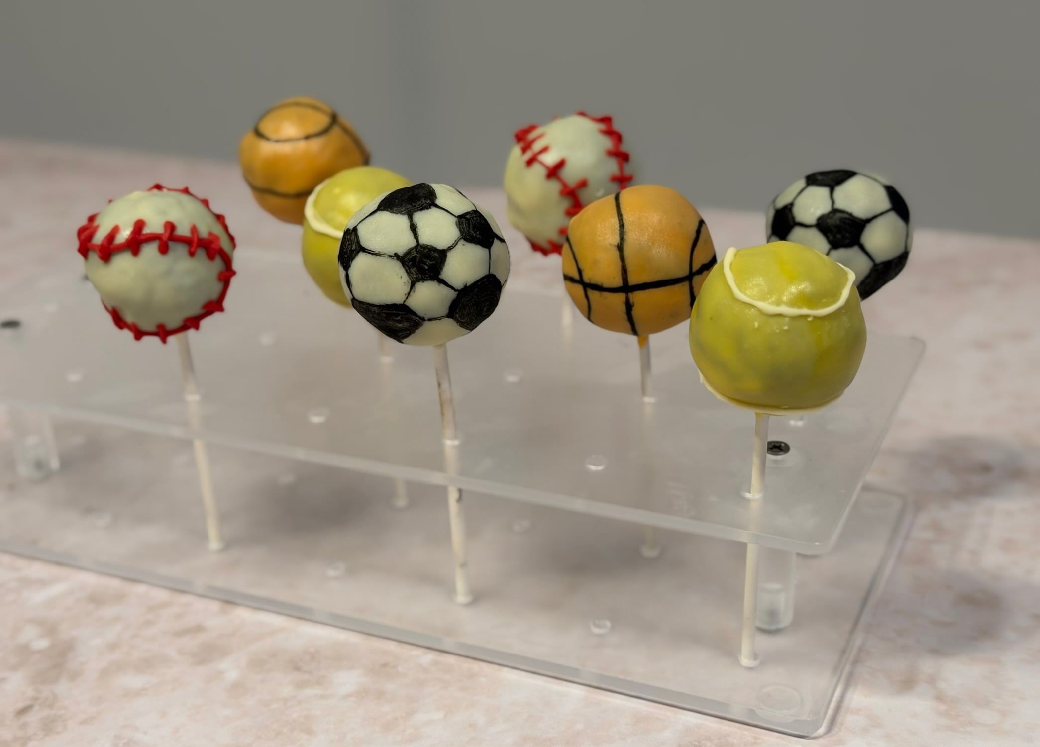Cake-Pops in Ballform auf einem Ständer: Fußball, Basketball, Tennisball und Baseball.