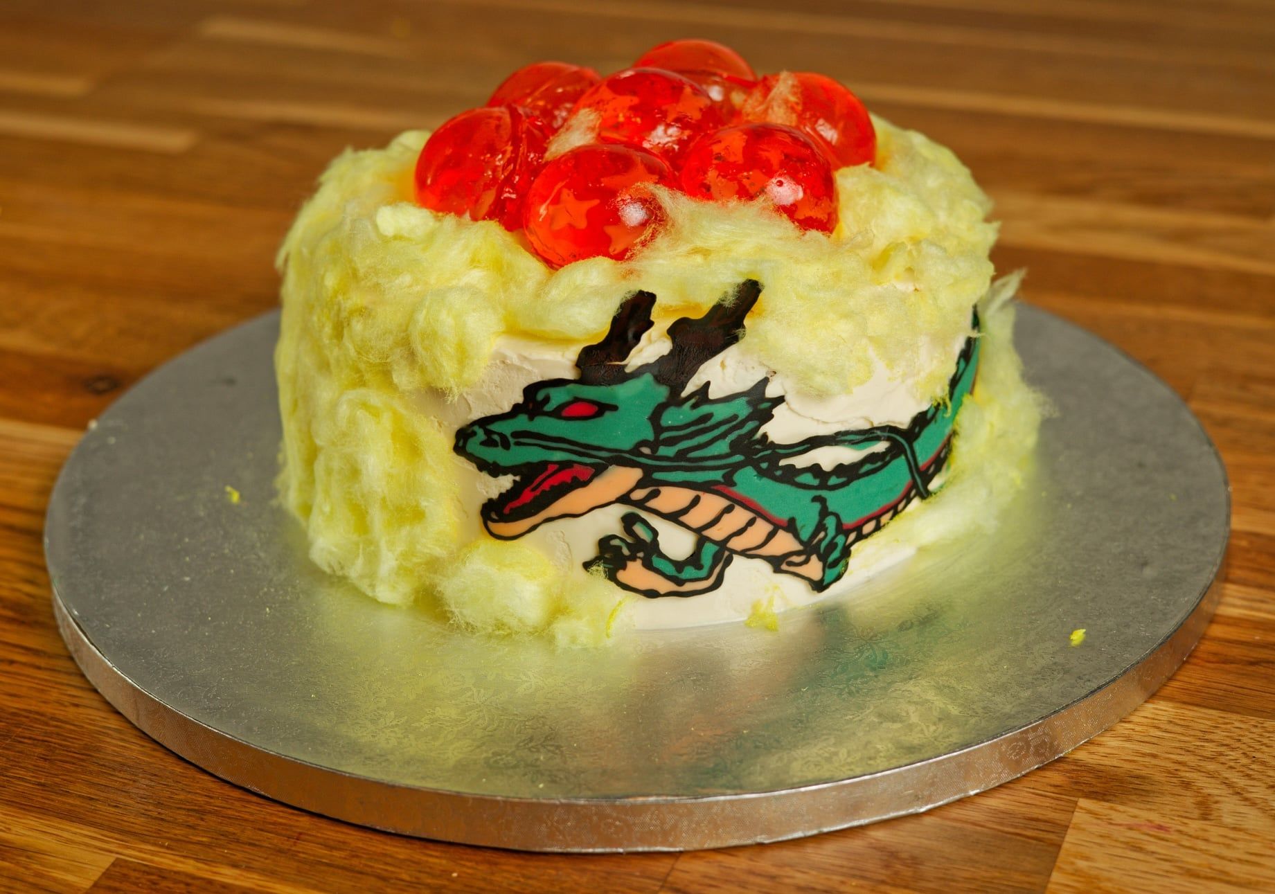 Runde Torte, um den Rand ein grüner Drache, Wolken aus heller Zuckerwatte, obenauf sieben rote Kugeln aus Götterspeise.
