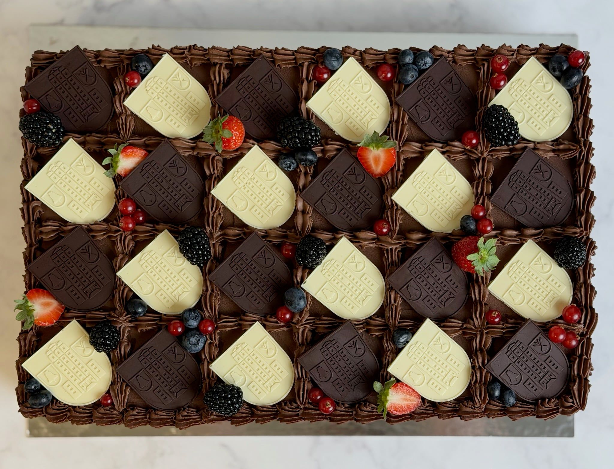 Dieselbe Torte von oben: die Wappen liegen in gleichmäßigen Reihen zwischen Buttercremetupfen und Beeren.
