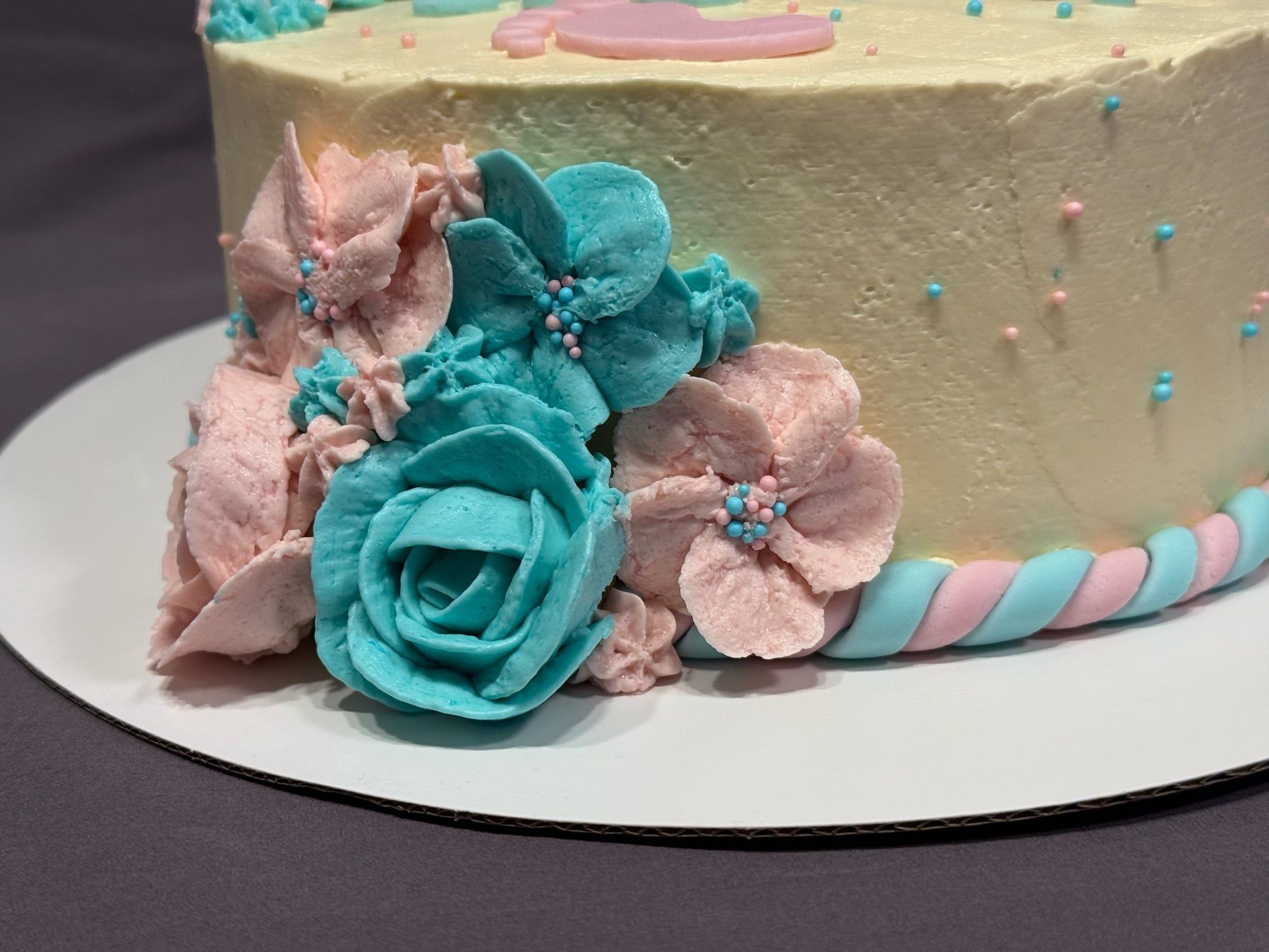 Seitenansicht: Buttercremeblüten in Rosa und Türkis, unten eine gedrehte Kordel in beiden Farben.